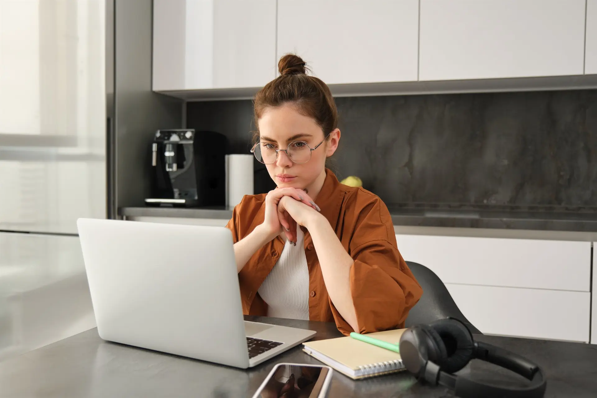 Remote support professional using a laptop and notebook to review recurring work and service plan priorities.